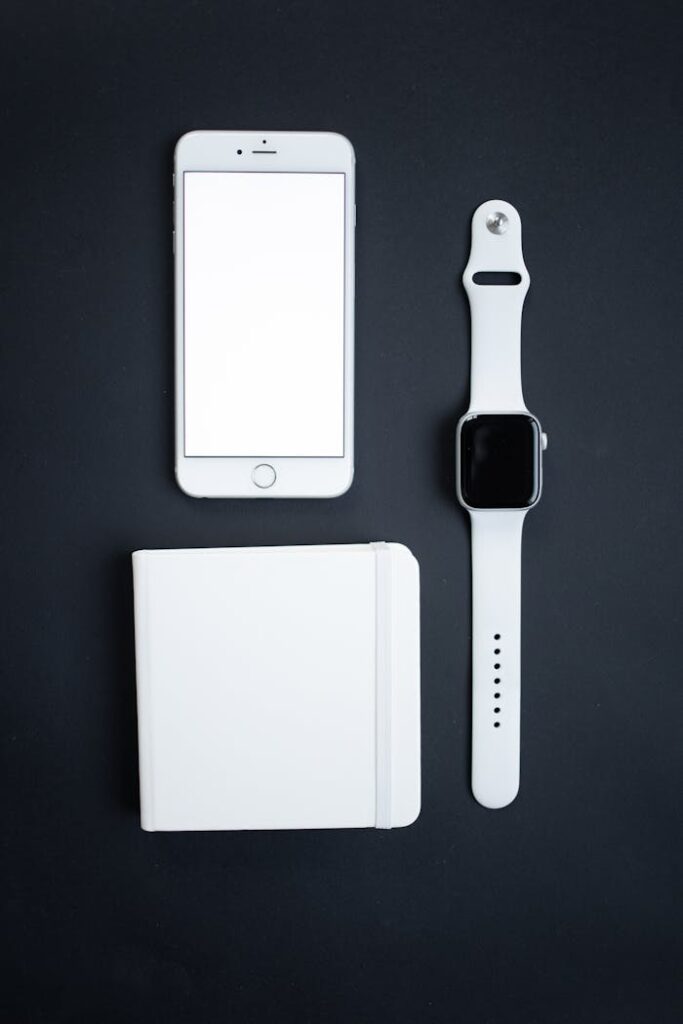 Minimalistic arrangement of a smartphone, smartwatch, and notebook on a black background.